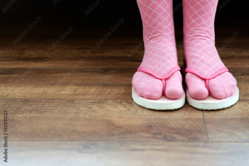 Female feet in socks with pink flip-flops, on floor background Female feet in socks with pink flip-flops, on floor background