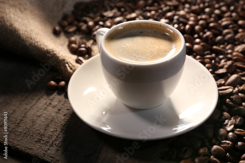 Cup of coffee and grains on wooden table with sackcloth,
