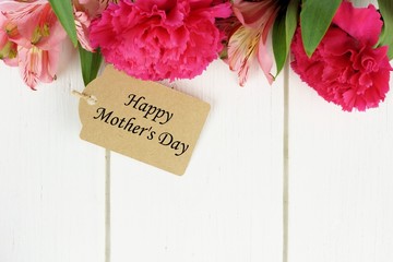Mother's Day gift tag amongst pink flowers against white wood