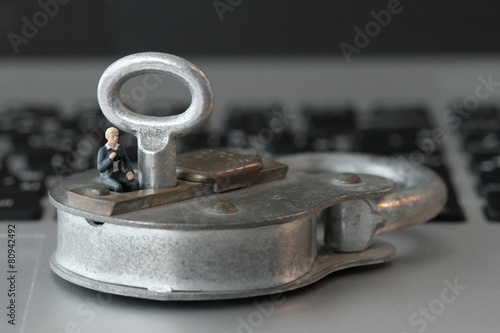 Internet security concept-miniature businessman sit on old key a
