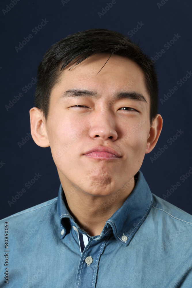 Fototapeta premium Pleased young Asian man making face and looking at camera