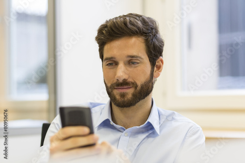 Cheerful Hipster man in office. Typing text on mobile phone