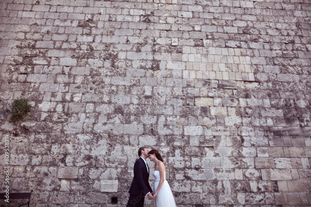 Bride and groom kissing near brick wall