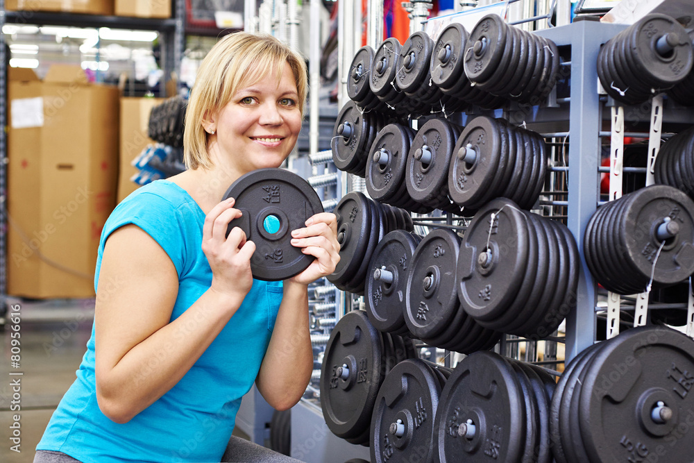 Happy woman chooses loads for dumbbell in sport shop Happy woman chooses loads for dumbbell in sport shop