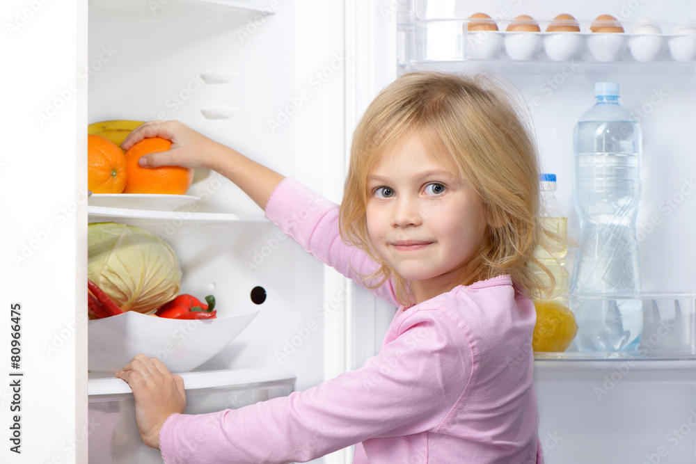Little girl looking at camera and picking food from fridge Little girl looking at camera and picking food from fridge