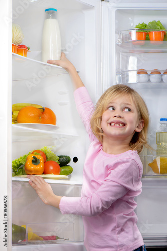 Funny smiling girl trying to pick food from fridge
