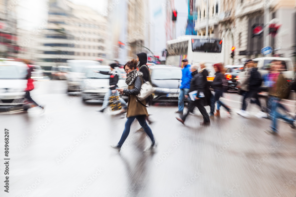 Menschenmenge überquert nasse Straße mit Zoomeffekt Menschenmenge überquert nasse Straße mit Zoomeffekt