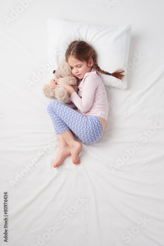 Top view of little cute girl sleeping with teddy bear
