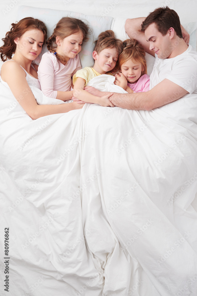 Family of five sleeping under blanket