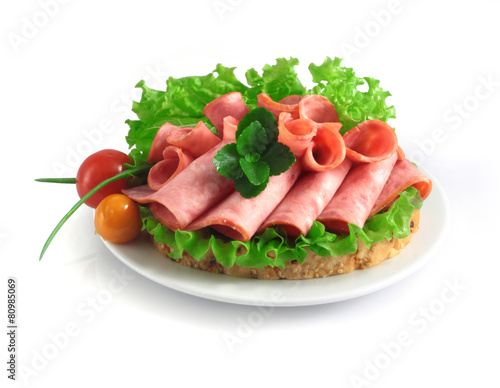 sliced sausage with herbs and vegetables on a white plate.