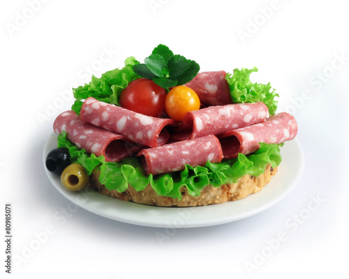 sliced sausage with herbs and vegetables on a white plate.