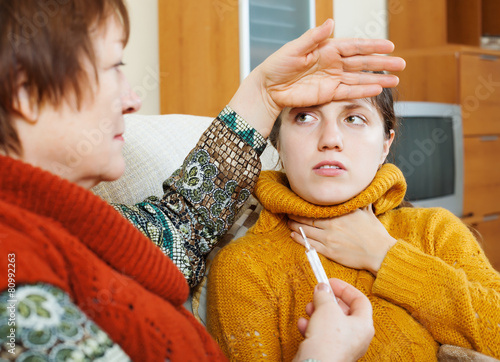  woman measuring temperature with thermometer for  adult daughte photo