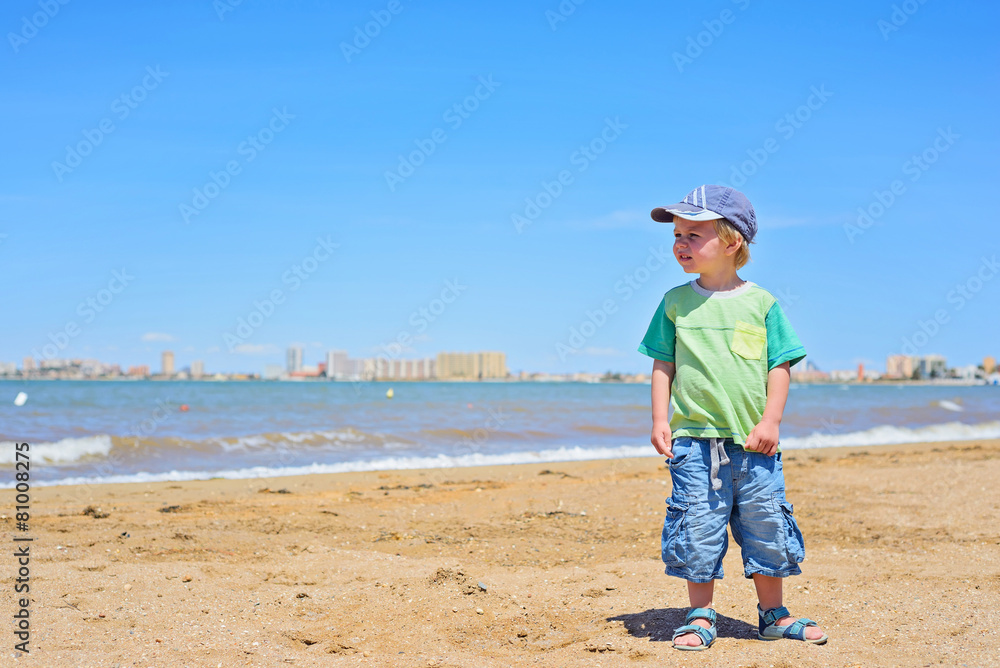 Small trendy boy standing sandy beach