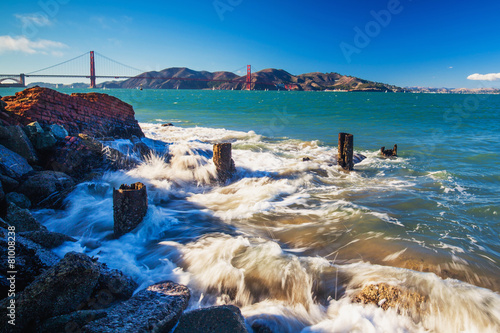 Surf splashes over rocks with the view of Golden Gate Bridge