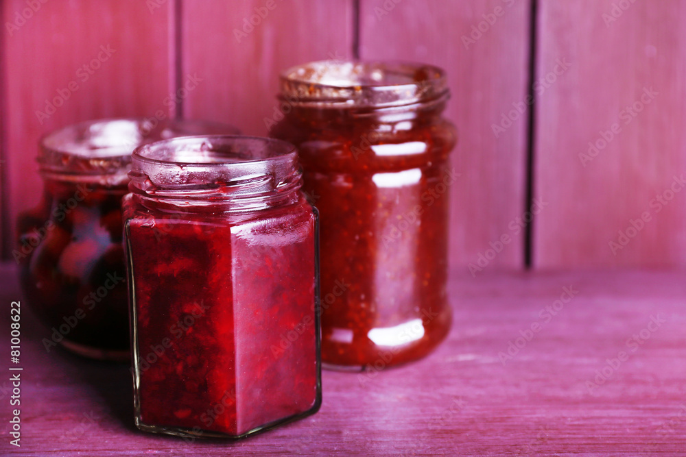 Homemade jars of fruits jam on color wooden background Homemade jars of fruits jam on color wooden background