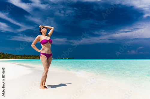 Woman in purple bikini covered in sand on tropical beach