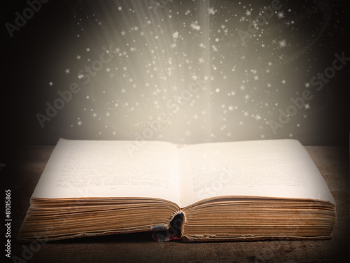 Old open book with magic light and falling stars