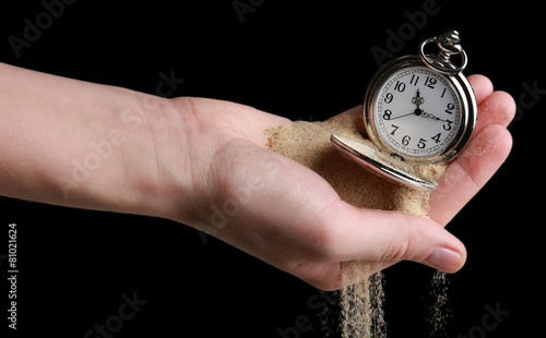 Silver pocket clock in hands and sand flowing away