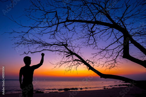 Silhouette man show his hand up in the air with dead tree at sun