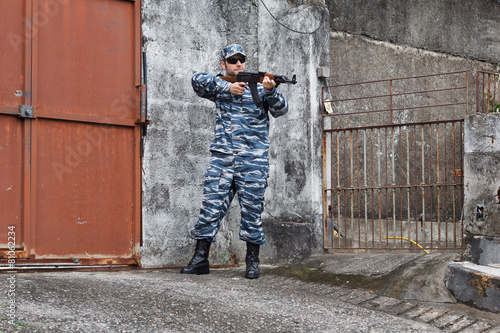 Caucasian military man in urban warfare protecting iron gate wit