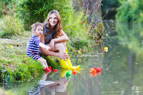 Adorable little girl and her mom playing with paper boats in a r photo