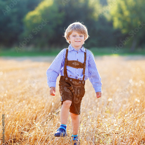 Funny little kid boy in leather shors, walking  through wheat fi photo