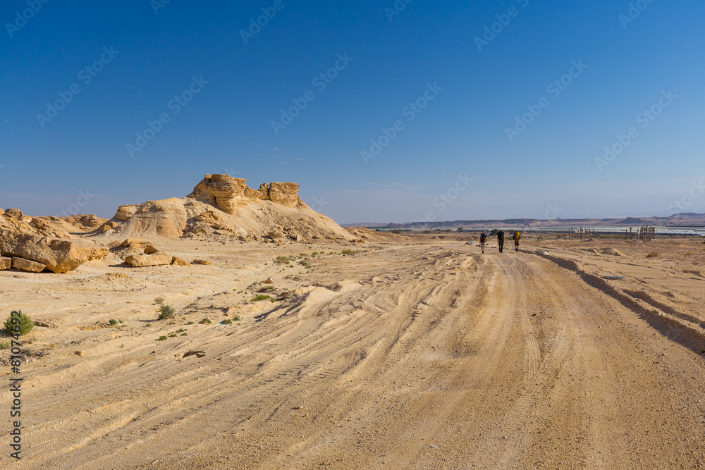 Backpackers walking desert road.