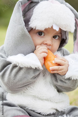 Pequeña bebé de seis meses disfrazada de coneja comiendo zanahorias photo