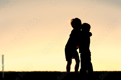 Silhouette of Two Young Children Hugging at Sunset