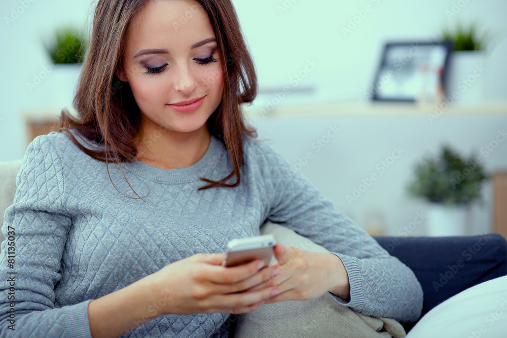 Pretty girl using her smartphone on couch at home in the living Pretty girl using her smartphone on couch at home in the living