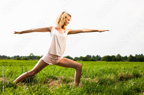 Beautiful young woman doing yoga exercise on field.