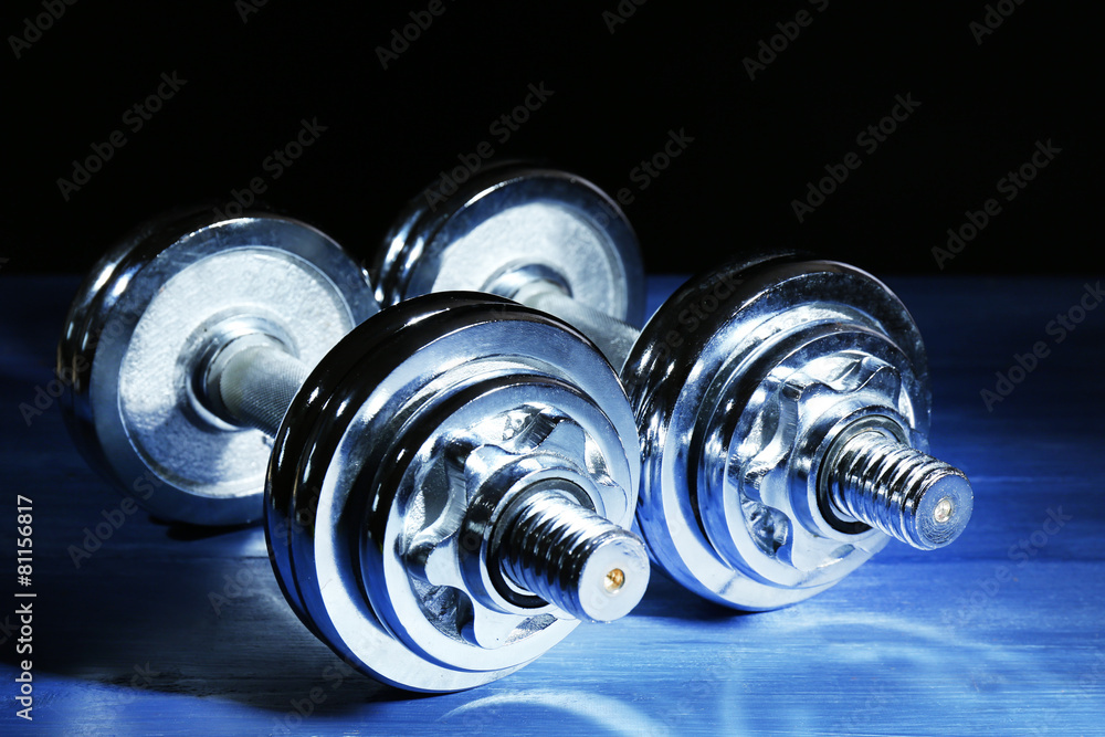 Dumbbells on color board, on dark background Dumbbells on color board, on dark background
