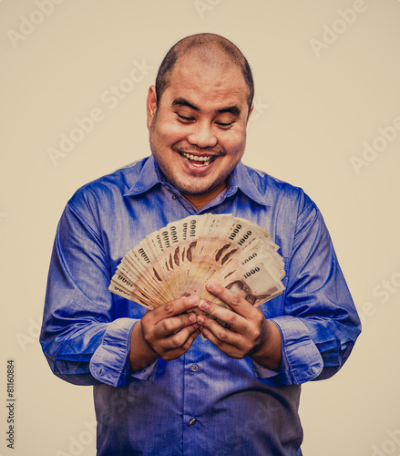 An office guy holding pile of Thai banknotes with his greedy fac