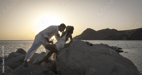 Silhouette of young couple on beach rocks at sunrise