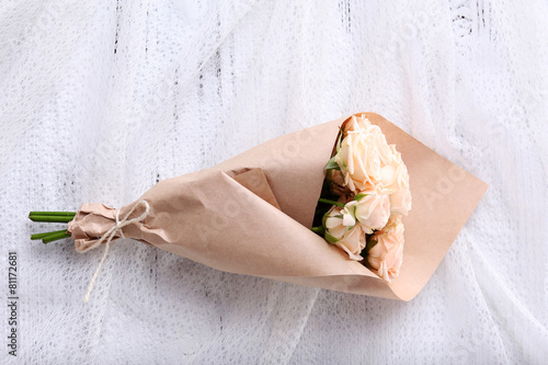 Bouquet of fresh roses wrapped in paper on wooden background
