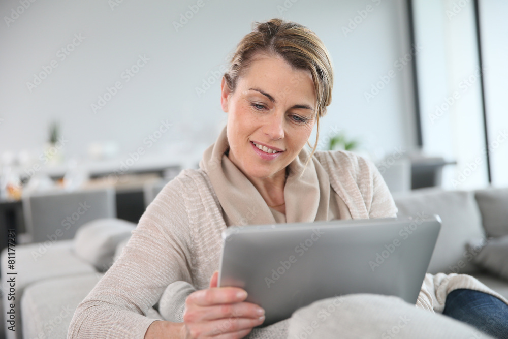 Mature woman sitting in sofa and websurfing with tablet Mature woman sitting in sofa and websurfing with tablet