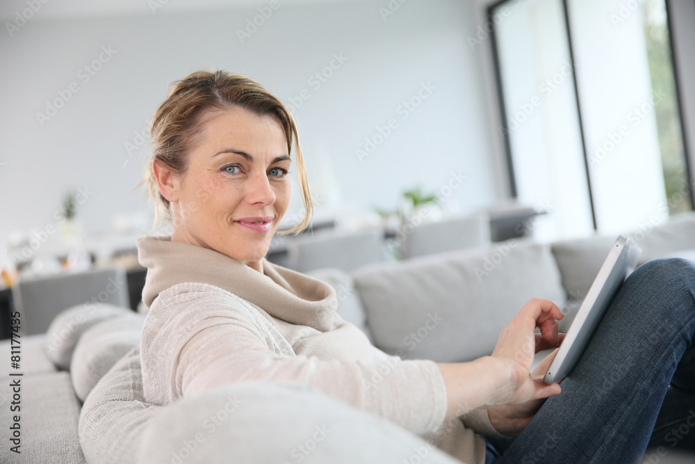 Mature woman sitting in sofa and websurfing with tablet Mature woman sitting in sofa and websurfing with tablet