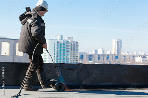 Roofer man worker installing roll of roofing felt