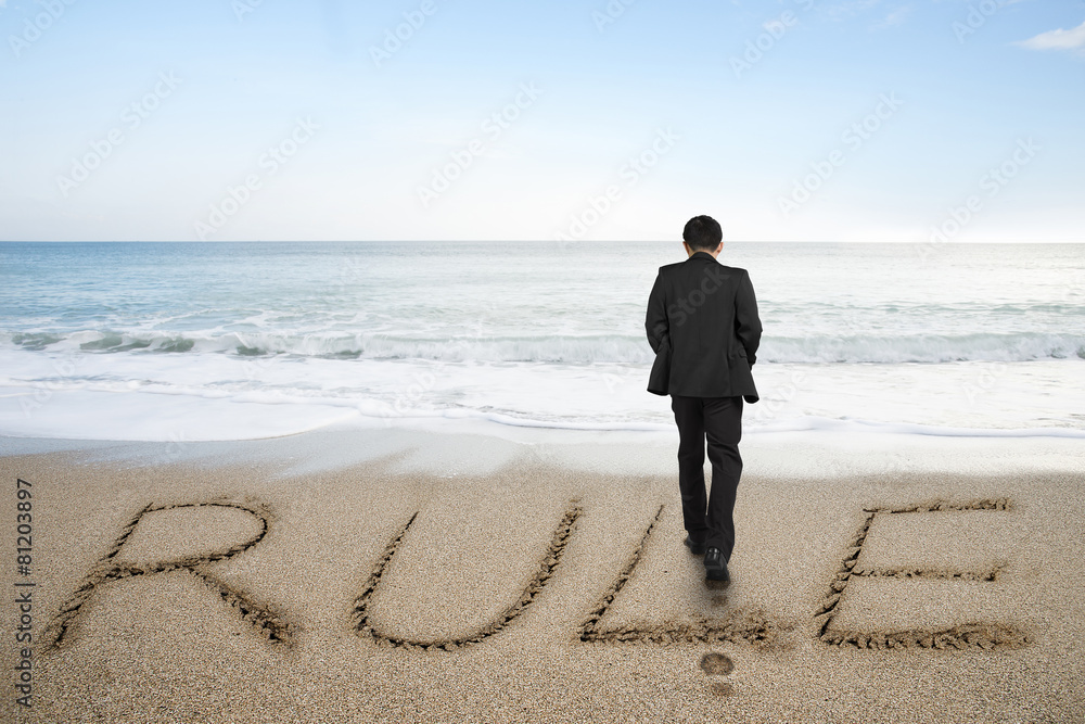 Rear view businessman standing with rule word on sand beach