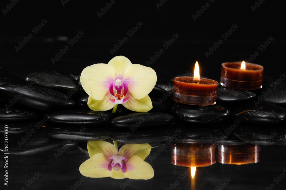 yellow orchid with two candle on therapy stones