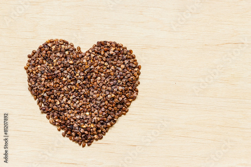 buckwheat groats heart shaped on wooden surface.