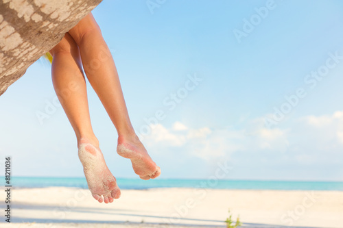 Woman sitting on palm tree at tropical beach