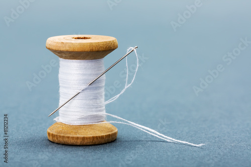 Spool of white sewing thread and needle