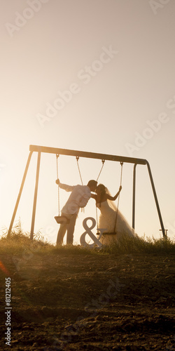 Silhouette of wedding couple kissing under swing set at sunset