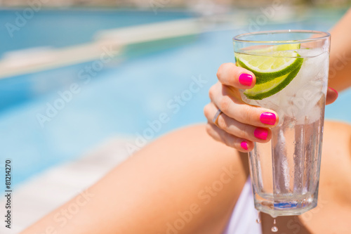 Photography Woman holding refreshing cold drink while sunbathing by the pool