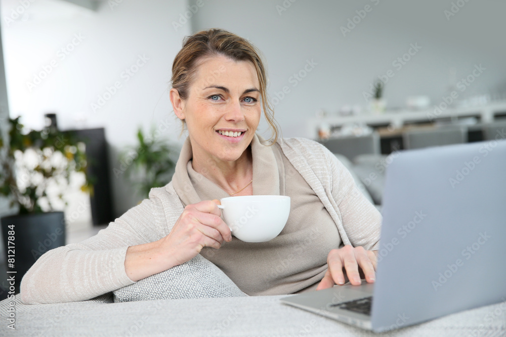 Mature woman relaxing with cup of coffee in front of laptop Mature woman relaxing with cup of coffee in front of laptop