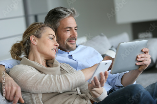 Mature couple at home using smartphone and tablet