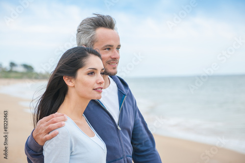 A beautiful couple is posing holding eachother at the beach