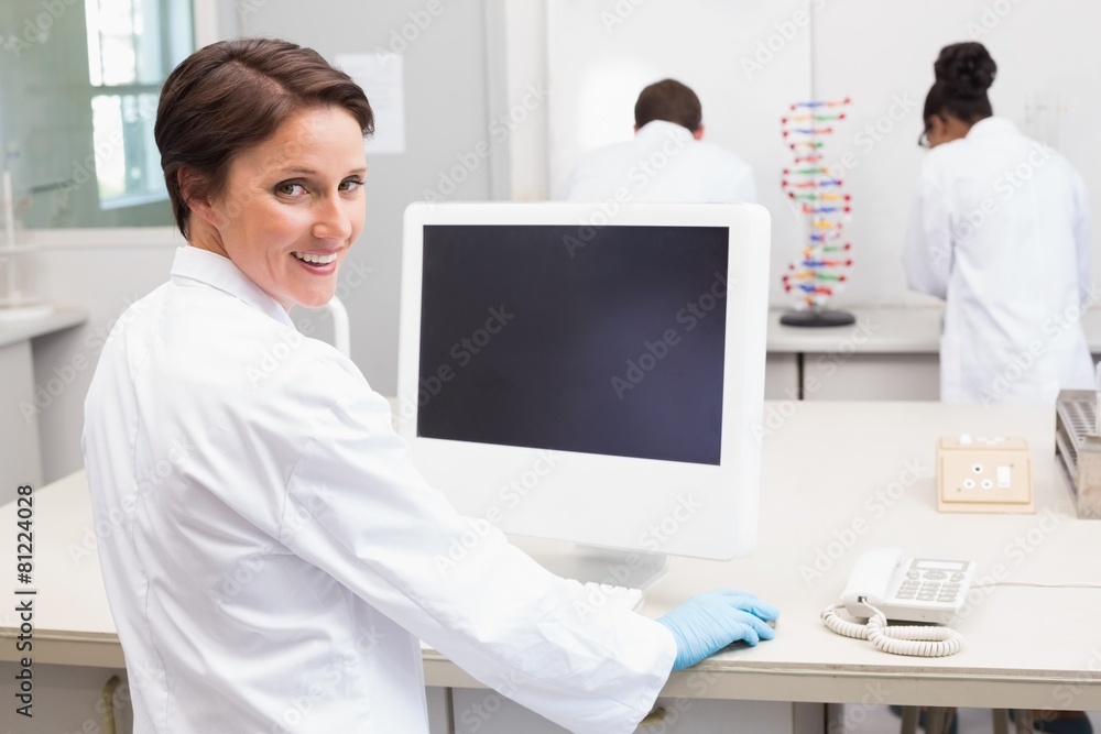 Smiling scientist using computer while colleagues working Smiling scientist using computer while colleagues working