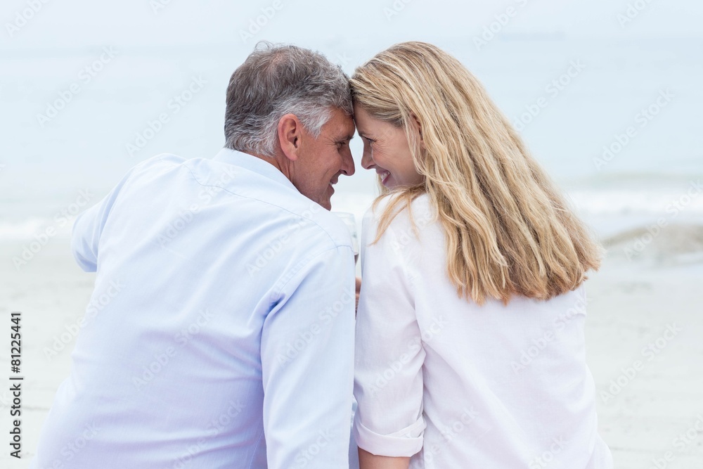 Happy couple sitting on the sand and smiling at each other